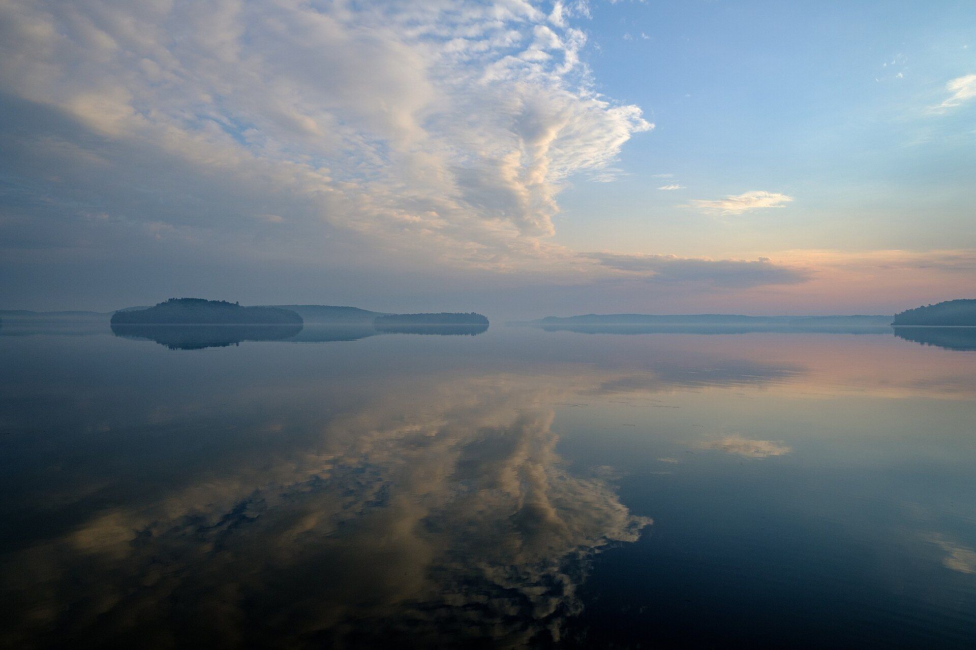 Calm sea reflecting a pale sky with soft clouds on the horizon